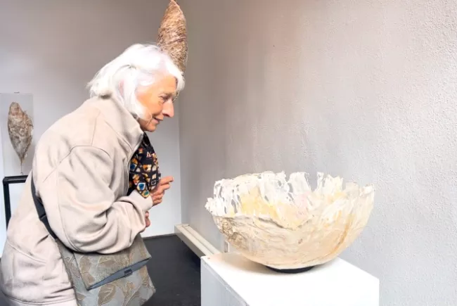 Un visiteuse qui admire une sculpture réalisée en papier, en forme de vase par l'artiste Viviane Fontaine
